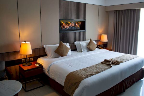 A neatly made bed with brown pillows and a gold accent blanket, nightstands with lamps on both sides, and a wall decoration above the headboard.