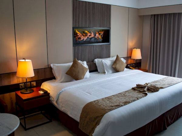 A neatly made bed with brown pillows and a gold accent blanket, nightstands with lamps on both sides, and a wall decoration above the headboard.