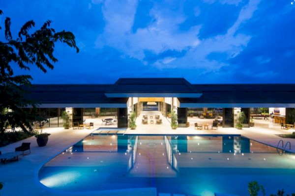 It's a luxurious outdoor pool area with modern architecture, illuminated at dusk or night under a striking blue sky.