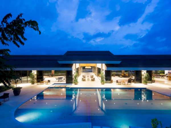 It's a luxurious outdoor pool area with modern architecture, illuminated at dusk or night under a striking blue sky.