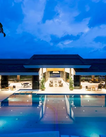 A luxurious outdoor pool area at dusk, with modern architecture, lounge seating, and ambient lighting under a twilight sky.