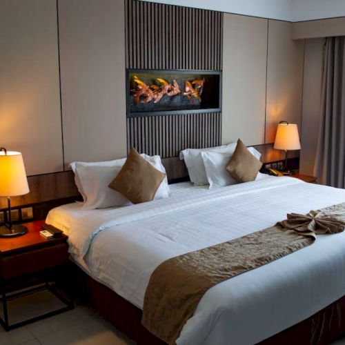 This image shows a neatly arranged hotel room featuring a large bed with white linens, bedside tables with lamps, and a decorative wall piece.