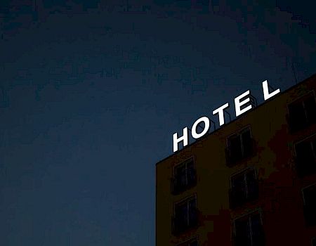 A building with a visible illuminated sign that reads "HOTEL" against a dark sky background is shown in the image.