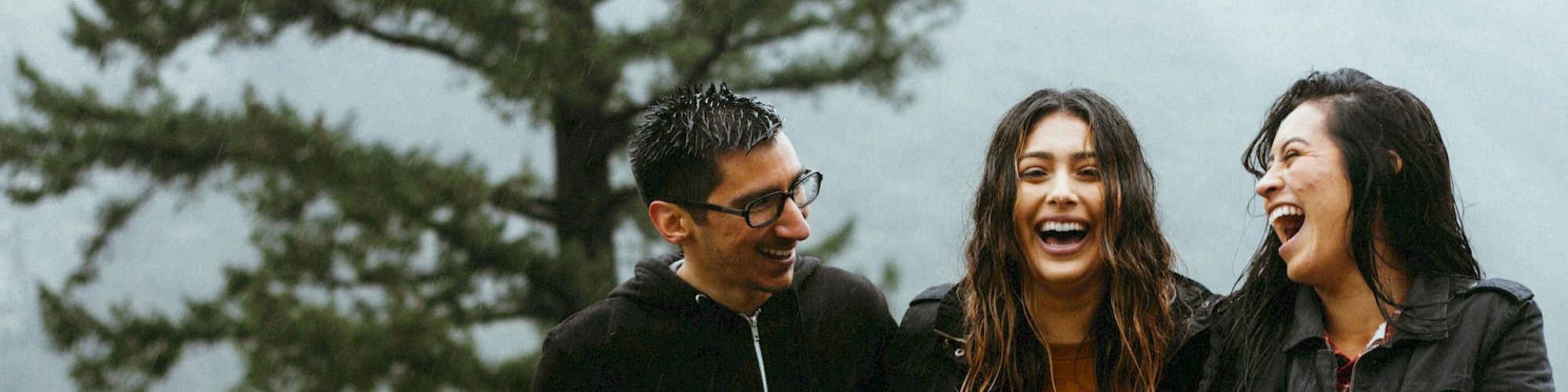 Three people are sitting on a stone ledge, laughing and enjoying themselves, with a blurred forest background.