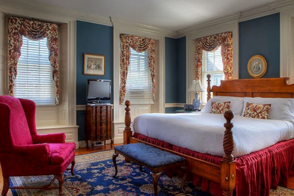 A bedroom with a large wooden bed, red armchair, small TV, decorative curtains, and blue walls, featuring traditional furniture and decor ending the sentence.