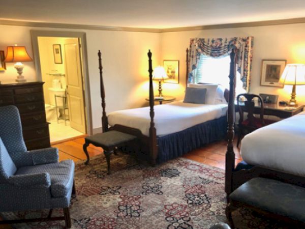 A cozy Newport, RI, guest room with a four-poseter queen-size bed, a twin-size bed, lamps, a blue armchair, and a dresser.