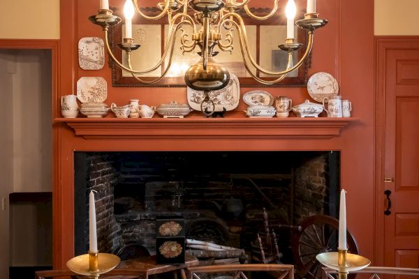 A dining room with a lit chandelier, a fireplace, a mirror, candlesticks, and tableware on a white tablecloth.