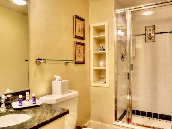 A bathroom with a shower with glass doors, a sink with a marble countertop, a toilet, and a small set of shelves.