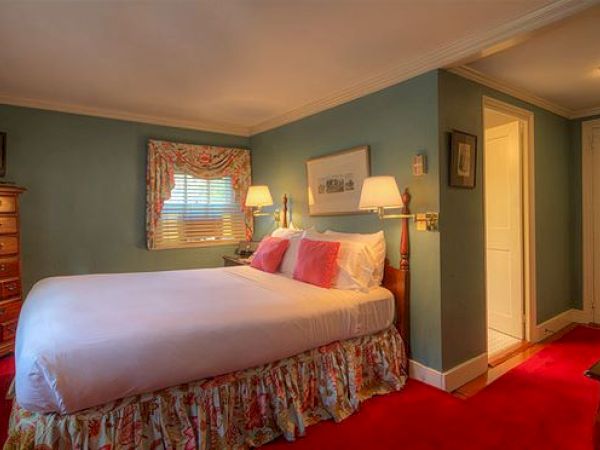 A cozy Newport, RI, guest room with a queen-size bed, a tall dresser, lamps, a desk, and a door leading to a private bath.