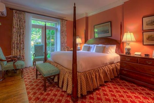 The image shows a cozy bedroom with a large bed, ornate decorations, bedside lamps, a dresser, and a window with curtains overlooking greenery.