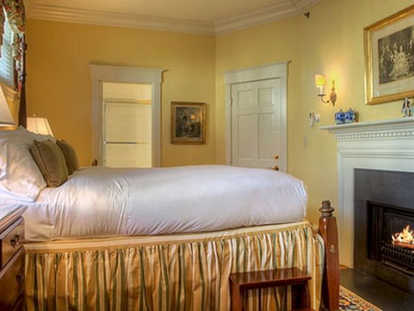 A cozy Newport, RI, guest room with a king-size bed, a gas fireplace, a dresser, and a door leading to a private bath.