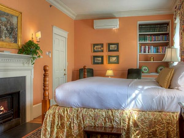 A cozy Newport, RI, guest room with a king-size bed, a gas fireplace, a book shelf, and a door leading to a private bath.