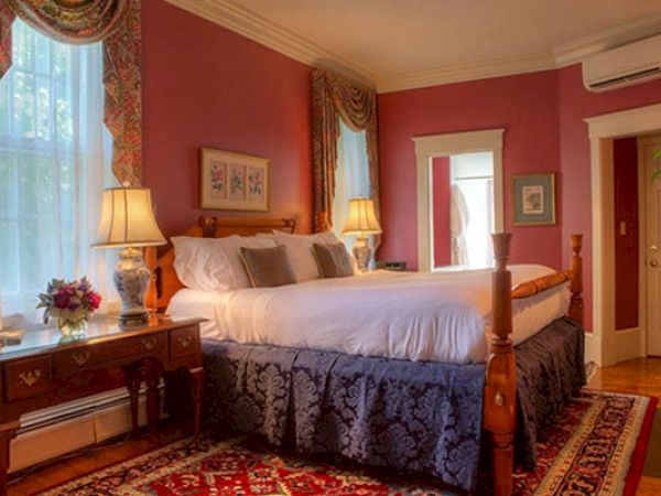 A cozy Newport, RI, guest room with a king-size bed, a gas fireplace, lamps, a desk, and a door leading to a private bath.