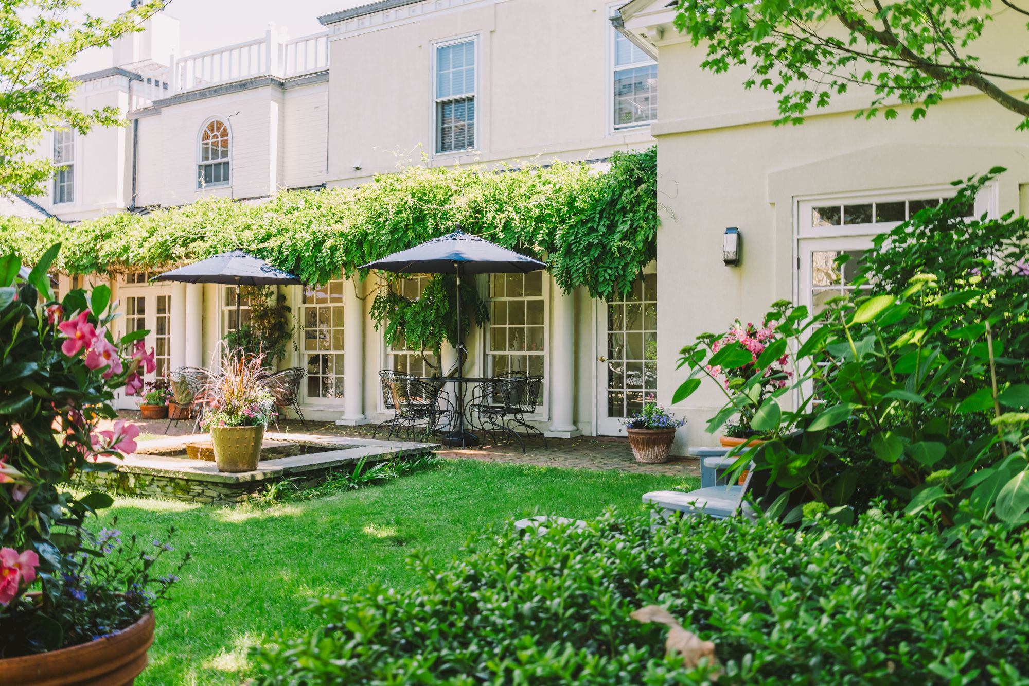 A lush courtyard garden with patio furniture and potted plants near ivy-covered walls and windows at The Francis Malbone House.