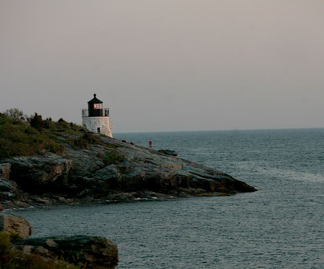 The image shows a lighthouse on a rocky coastline with the sea in the background and a serene, early evening sky.