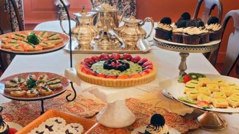 An elegant table setup featuring assorted pastries, tarts, cupcakes, and silver tea sets ready for a high tea or dessert gathering.