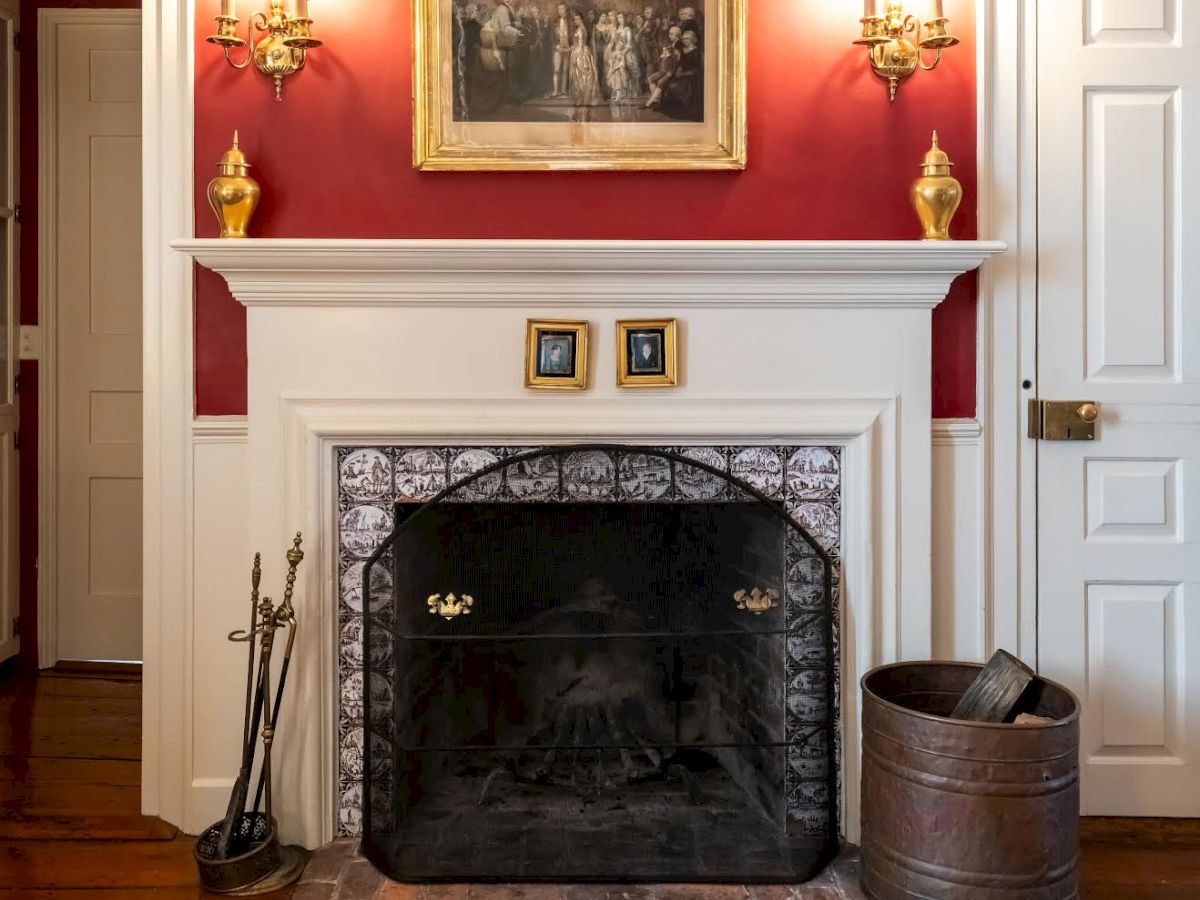 A red-walled room featuring a fireplace, two sconces, a framed picture above, doors on either side, a black fireplace cover, and a patterned rug.