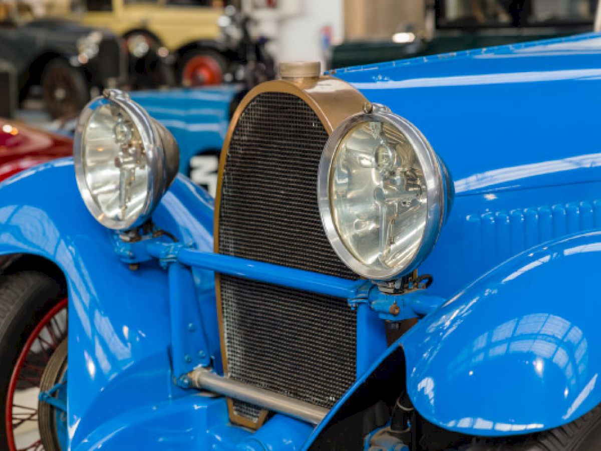 A close-up of the front of a vintage blue car, showcasing its headlights, radiator grille, and classic lines.
