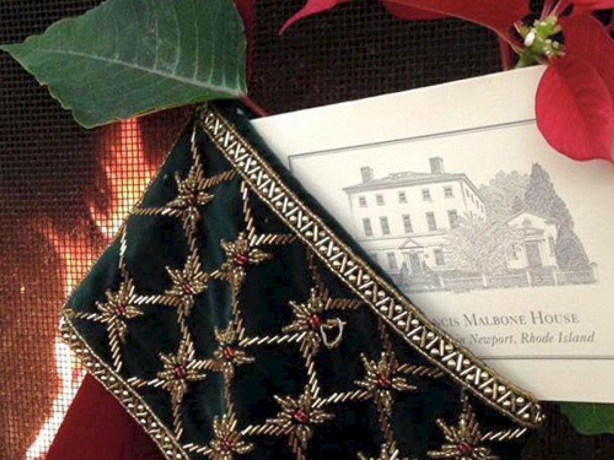 A beaded bag, a postcard from Francis Malbone House in Newport, RI, and a poinsettia plant are in front of a cozy fireplace.