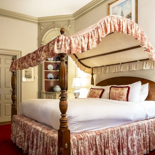 A guest room with a canopy bed, ornate bedspread, decorative pillows, and elegant decor, featuring a lamp and framed artwork.