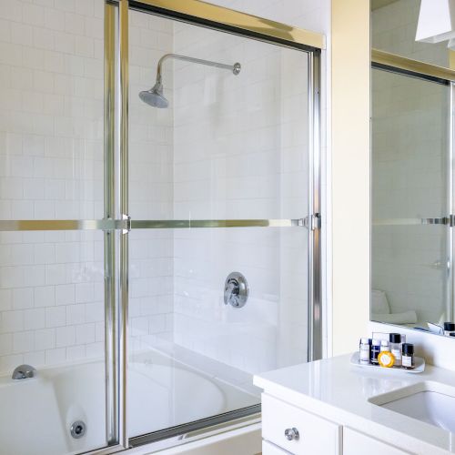 A bathroom featuring a bathtub with sliding glass doors, showerhead, a sink with a countertop, and toiletries.