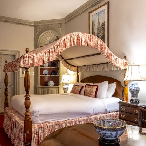 The image depicts a luxurious bedroom with an ornate four-poster bed, antique furniture, elegant table, china set, table lamps, and framed artwork on the wall.