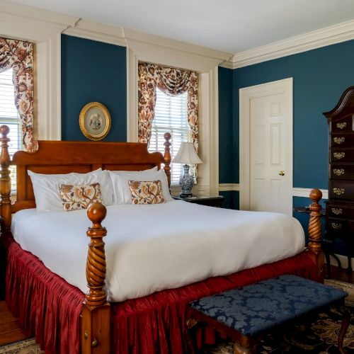 A cozy bedroom with a large wooden bed, two bedside tables, lamps, ornate curtains, and a matching dresser and bench.