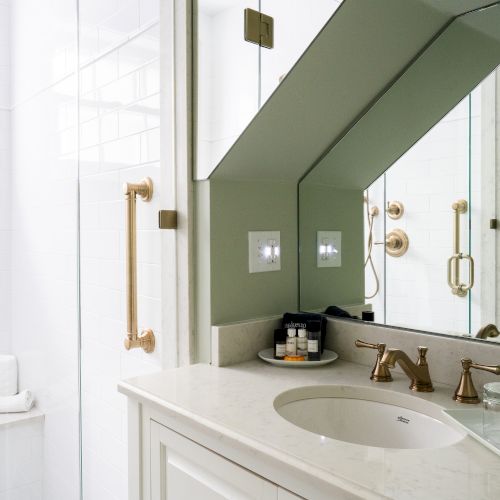 A clean, modern bathroom featuring a glass shower with brass fixtures, a sink vanity with a mirror, and wall-mounted toiletries.