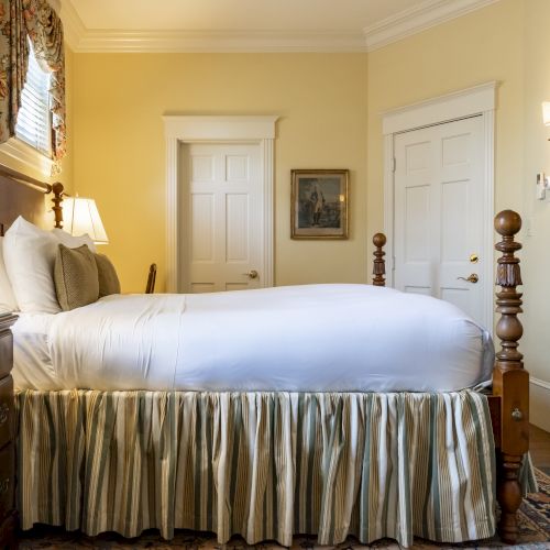 A cozy bedroom with a neatly made bed, elegant bedside lamps, a dresser, a fireplace, and framed artwork on a light yellow wall ending the sentence.