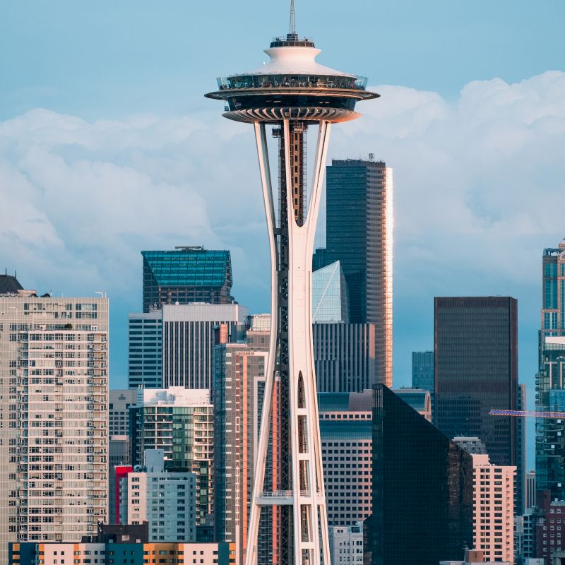 The image features the iconic Space Needle tower located in Seattle, surrounded by downtown skyscrapers under a blue sky with scattered clouds.