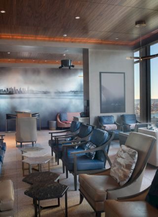 A modern lounge area featuring comfortable seating, a mural of a cityscape, large windows offering a view of the waterfront, and soft lighting.