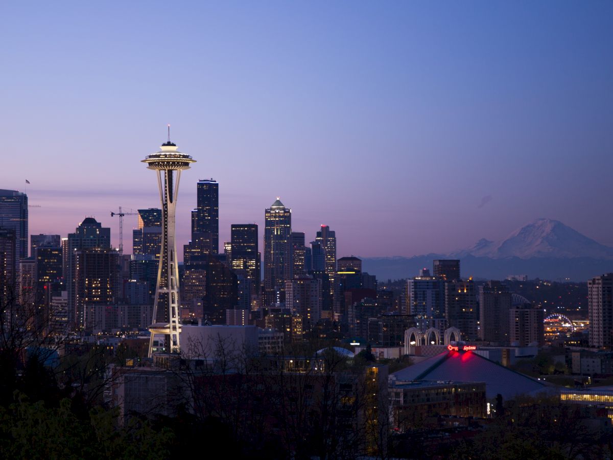 The image shows a city skyline at dusk with the Space Needle prominently featured and Mount Rainier visible in the background.