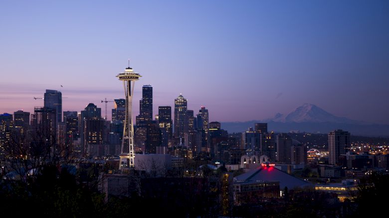 The image shows a city skyline at dusk with the Space Needle prominently featured and Mount Rainier visible in the background.